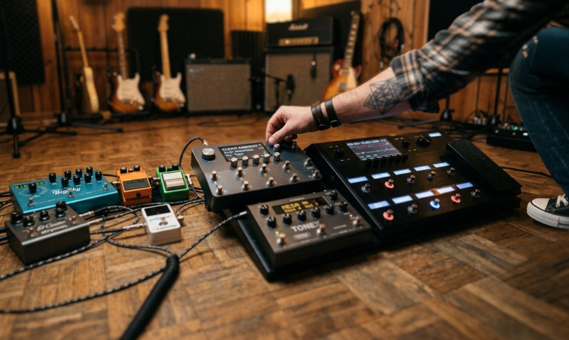 Person adjusting guitar effect pedals on a wooden floor with musical equipment in the background.